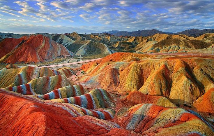 Pemandangan Lembah Pelangi di Pulau Hormuz dengan tanah berwarna merah, kuning, dan ungu akibat mineral alami.