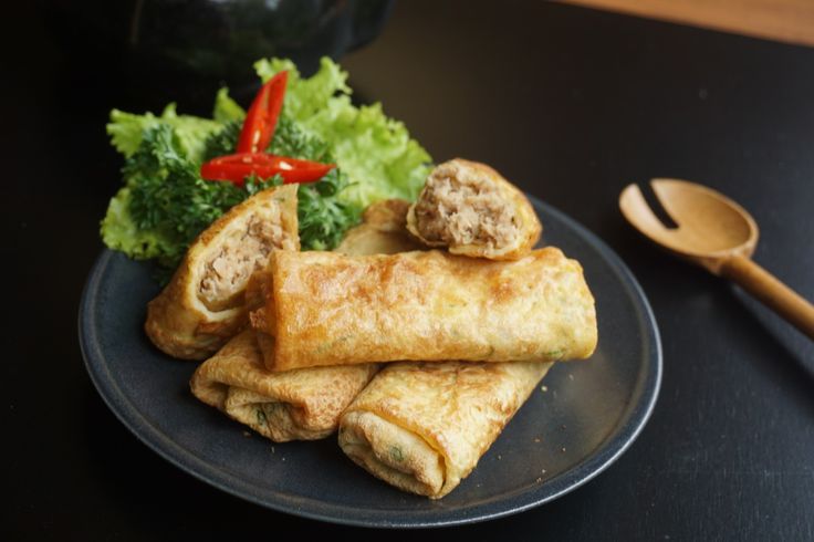 Foto Sosis Solo dengan kulit dadar tipis berwarna keemasan, diisi daging cincang berbumbu rempah, disajikan di atas piring dengan cabai rawit merah sebagai pelengkap.