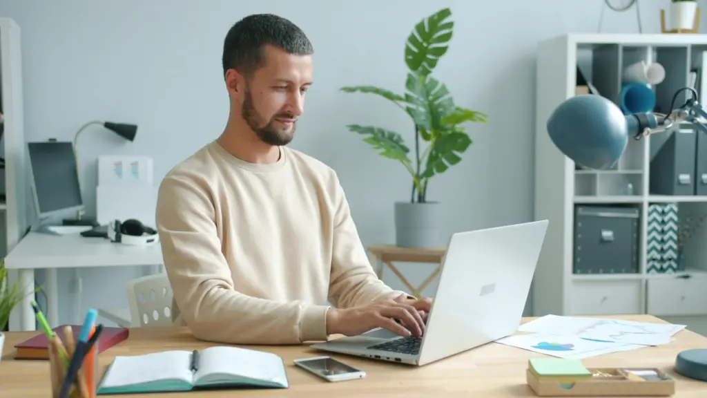 Seorang profesional muda sedang fokus bekerja di depan laptop dengan buku catatan, ilustrasi strategi membangun reputasi profesional yang solid.